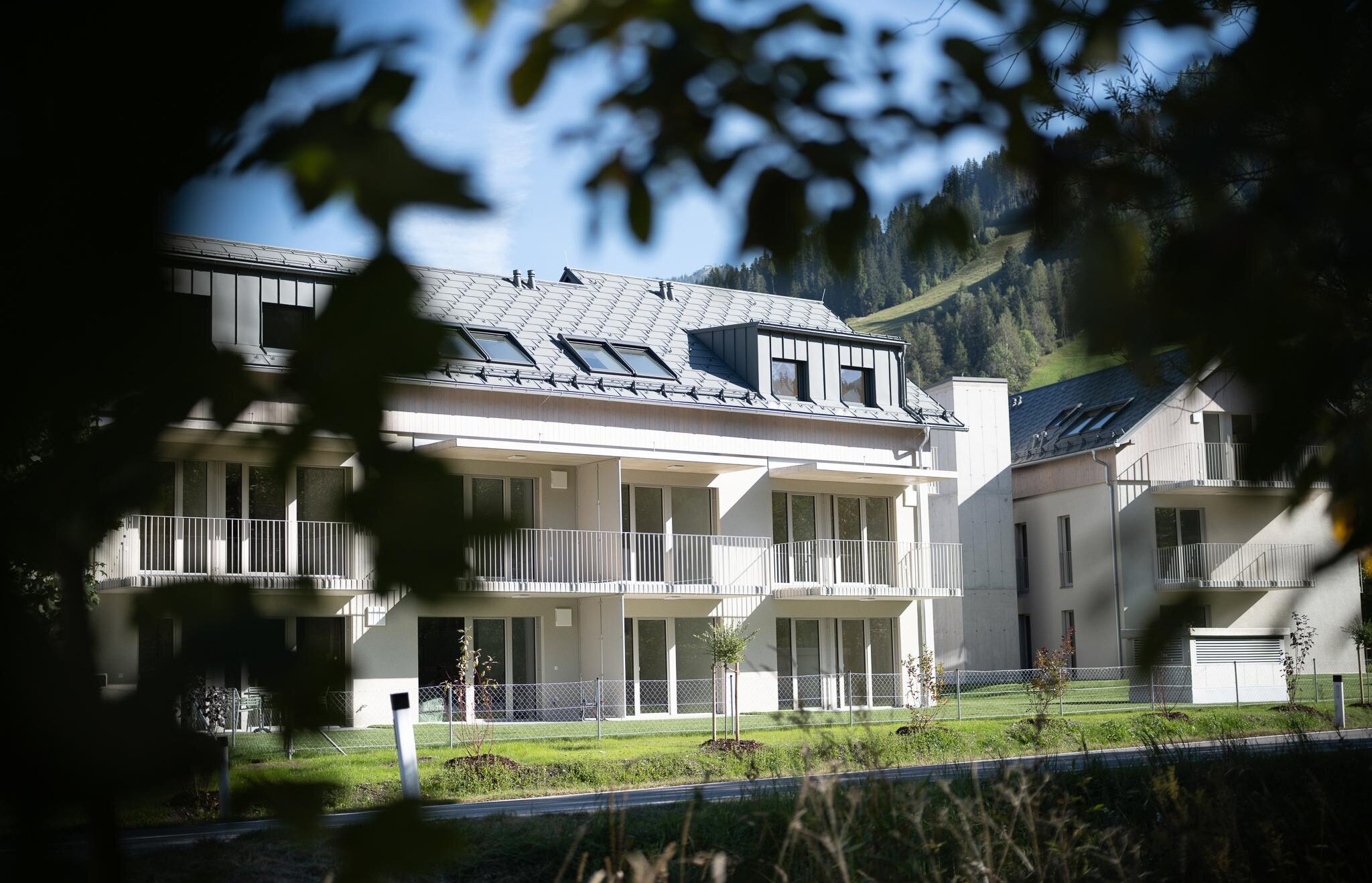 Moderne weiße Wohnanlage mit Balkonen, eingerahmt von Bäumen