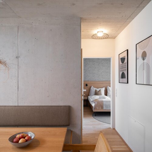 Dining area beside concrete wall, view into bedroom