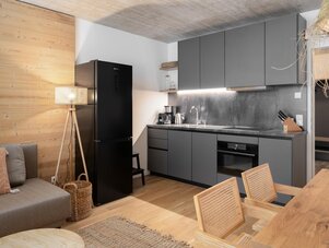 Open-plan kitchen with grey cabinets and black fridge, adjacent living area