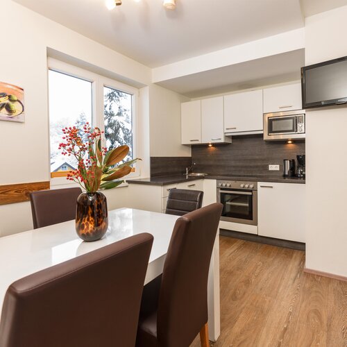 Modern kitchen with white cabinets, dining table, and TV