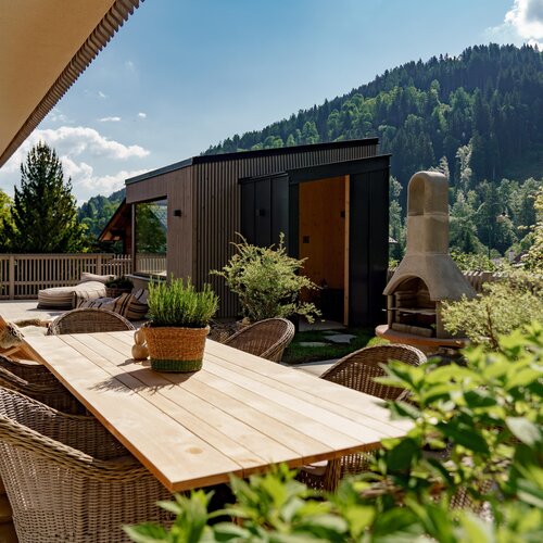 Sonnenbeschienene Terrasse mit Holztisch, Korbstühlen und Pflanzen