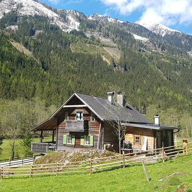 Holzhaus im Alpenstil auf grünem Weideland mit schneebedeckten Gipfeln