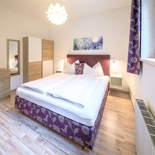 Helles, modernes Schlafzimmer mit lila Bettgestell im Blütenmuster