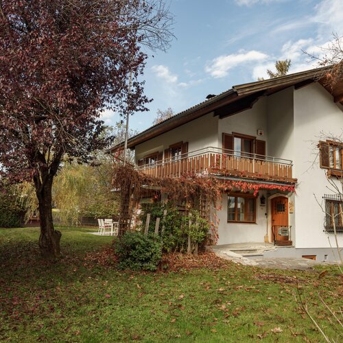 Zweistöckiges weißes Haus mit Holzbalkon und Herbstgarten