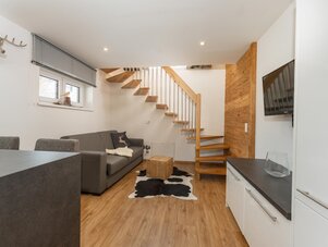 Gemütliches Wohnzimmer mit grauer Couch und Holztreppe