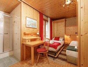 Holzverkleidetes Hotelzimmer mit zwei Betten, Schreibtisch und Dusche