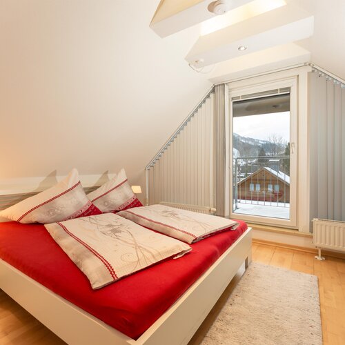 Bright modern bedroom with red bedding, slanted ceiling, balcony view
