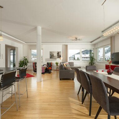 Offener Küchen-, Ess- und Wohnbereich mit großen Fenstern.
