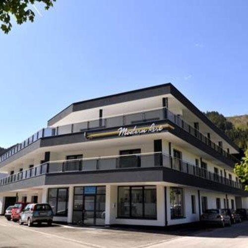 Dreistöckiges modernes Gebäude mit Balkonen und Parkplatz.