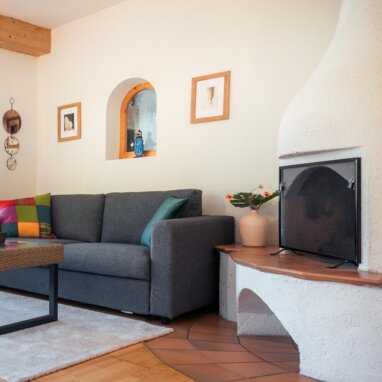 Wohnzimmer mit grauer Couch, Sessel und Kamin. | © TIEBER