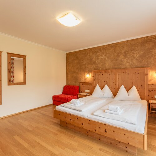 Hotelzimmer aus Holz mit Doppelbett und roter Sitzecke