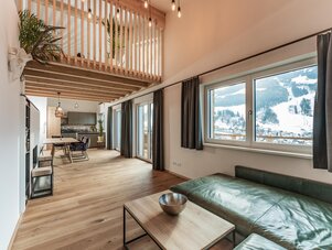 Offener Wohnbereich mit Sofa, Esstisch und Mezzanin mit großen Fenstern