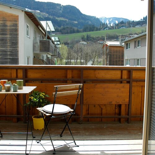Balkon mit Holzgeländer, Tisch mit Topfpflanzen und Bergblick.