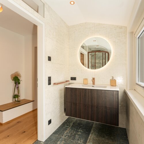 Modernes Badezimmer mit rundem, beleuchtetem Spiegel und dunklem Waschtisch