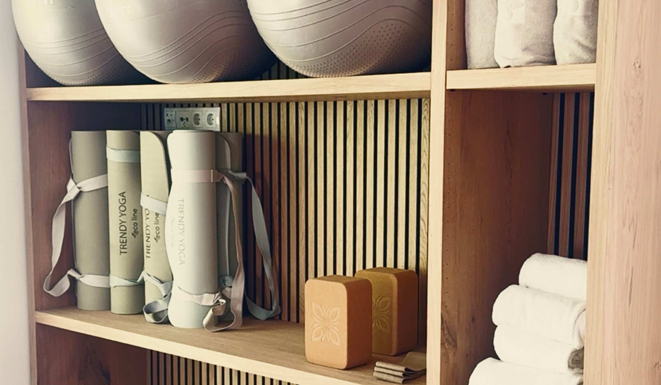 Holzregal mit Fitnessausrüstung: Bälle, Matten und Handtücher.