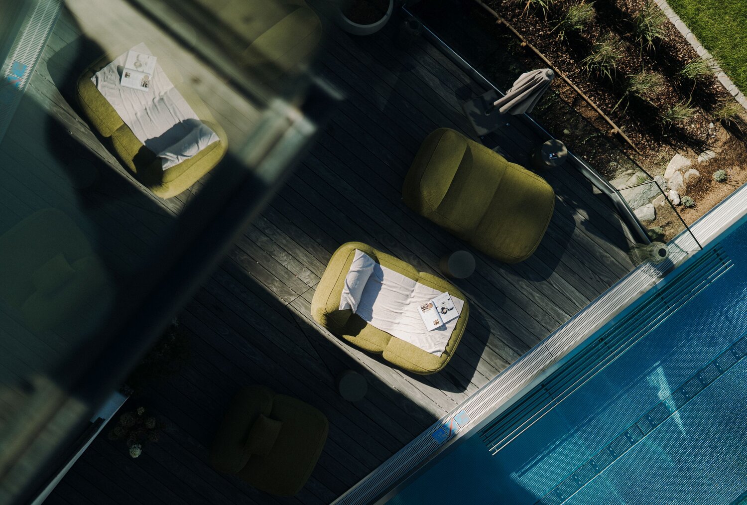 Luftaufnahme einer Poolterrasse mit grünen Loungesesseln und Magazinen