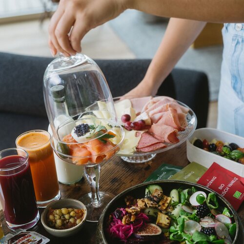 Hands arranging a brunch spread with fruit, cheese and meats.