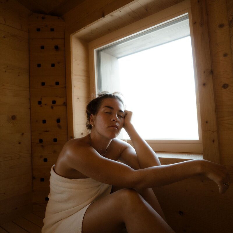 Young woman seated in a towel in a wooden sauna by window